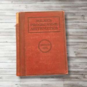 Peut inclure: Un livre rouge vintage intitulé "Milne's Progressive Arithmetics Complete Book". Le livre a un aspect usé et vieilli et est probablement un manuel scolaire.