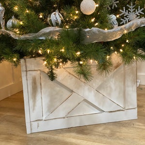 Puede incluir: Un soporte de árbol de Navidad de madera blanca con un diseño de cruz. El soporte está desgastado y tiene un aspecto rústico.