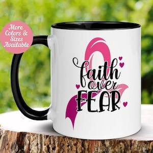May include: White coffee mug with a black handle and black rim. The mug has a pink ribbon design with the text "faith over FEAR" and small pink hearts.
