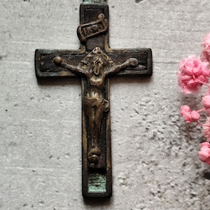 May include: A vintage bronze crucifix pendant featuring a detailed figure of Jesus Christ on the cross. The cross has a patina finish and a small loop at the top for hanging.