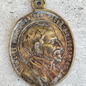 Peut inclure: Un pendentif ovale en bronze vieilli avec une boucle en haut. Il présente un profil détaillé d'un homme et est inscrit avec du texte sur le bord. La couleur générale est un bronze chaud et vieilli.