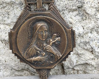 May include: A bronze religious plaque with a depiction of the Virgin Mary holding a rose. The plaque is octagonal and features a cross at the top.