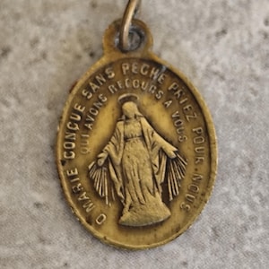 Peut inclure: Pendentif ovale doré vintage à thème religieux. Le pendentif présente une image d'une figure aux bras tendus, entourée de texte. Le texte se lit « O Marie conçue sans péché, priez pour nous qui avons recours à vous. »