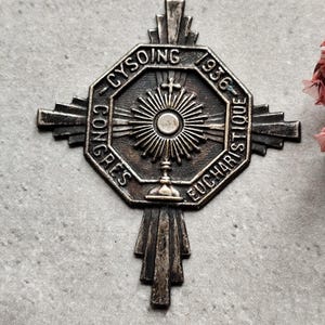 Könnte beinhalten: Eine silberfarbene religiöse Medaille mit einem Kreuz und einem Sonnenstrahl-Design. Die Medaille ist mit dem Text "Congres Eucharistique - Cysoing 1936" beschriftet.