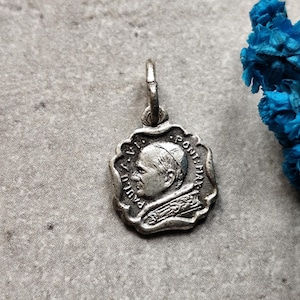 Pode incluir: Pingente de prata com um perfil do Papa Paulo VI, com a inscrição "PAUL VI PONT. MAX." ao redor da borda.