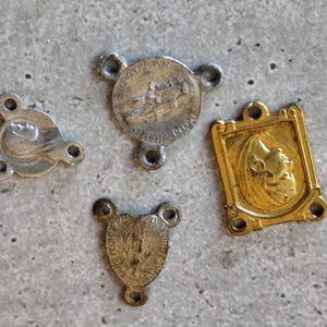 Könnte beinhalten: Vier antike religiöse Anhänger und Medaillons. Die Anhänger sind aus silber- und goldfarbenem Metall gefertigt. Die Anhänger umfassen einen runden Anhänger mit einem Bild eines Bootes, einen herzförmigen Anhänger und zwei weitere Anhänger mit religiösen Bildern.