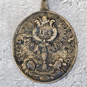 Peut inclure: Une médaille en laiton ovale vintage avec un motif religieux. La médaille représente l'Eucharistie, un calice et une hostie. L'inscription sur la médaille est "I.H.S.S.A.C."