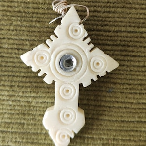 Può includere: Ciondolo in osso bianco a forma di croce con un design circolare e un anello in metallo argentato.