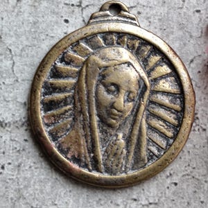 Peut inclure: Un pendentif rond en laiton représentant une image en relief de la Vierge Marie avec une auréole. Le pendentif a une boucle en haut pour l'accrocher.