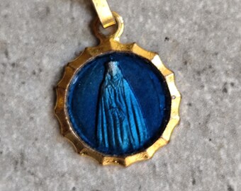 Puede incluir: Colgante dorado con un centro de esmalte azul que representa una figura religiosa. El colgante tiene un borde festoneado y un pequeño lazo para una cadena. La figura está representada con túnicas azules.