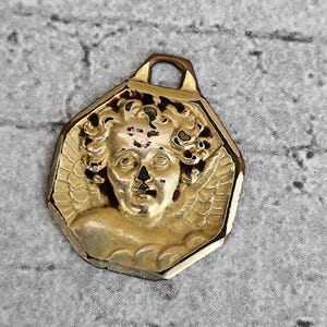 Antieke religieuze medaille met een cherubijn en engel Rafaël in goudkleur