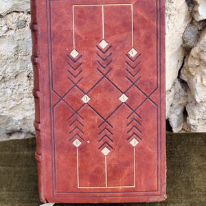 May include: A brown leather-bound book with a geometric design on the cover. The design features a series of white diamonds and arrows.