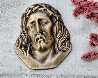 Könnte beinhalten: Eine goldfarbene Metallsculptur eines Männergesichts mit einer Dornenkrone. Die Skulptur ist detailliert und realistisch, mit einem traurigen Ausdruck.