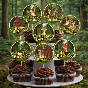 May include: A tiered dessert stand holds chocolate cupcakes topped with chocolate frosting. Each cupcake is decorated with a circular topper featuring characters and the words "Happy Birthday". The background is a blurred forest scene.