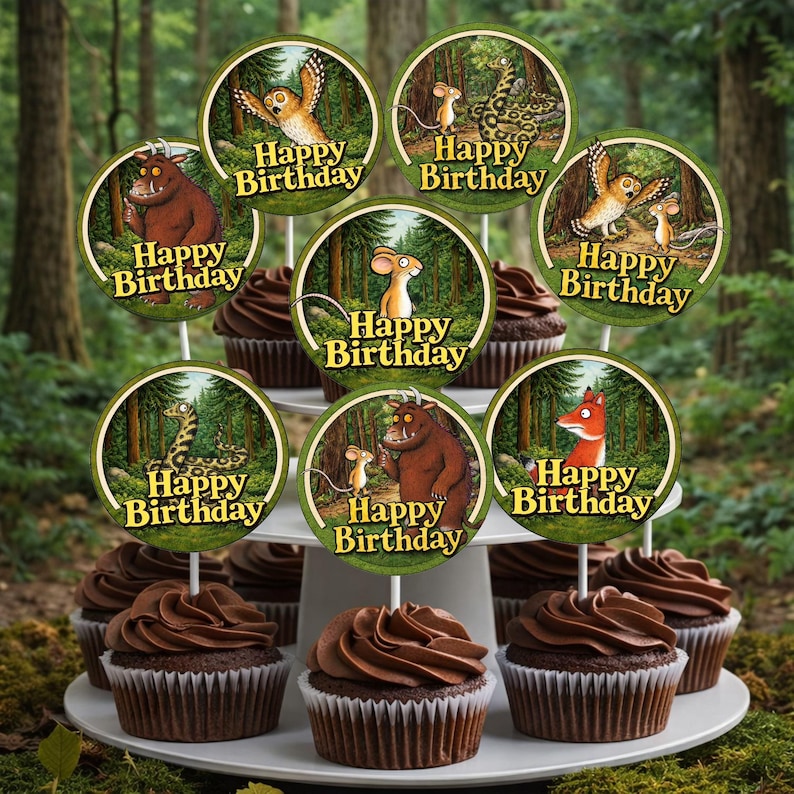 May include: A tiered dessert stand holds chocolate cupcakes topped with chocolate frosting. Each cupcake is decorated with a circular topper featuring characters and the words "Happy Birthday". The background is a blurred forest scene.