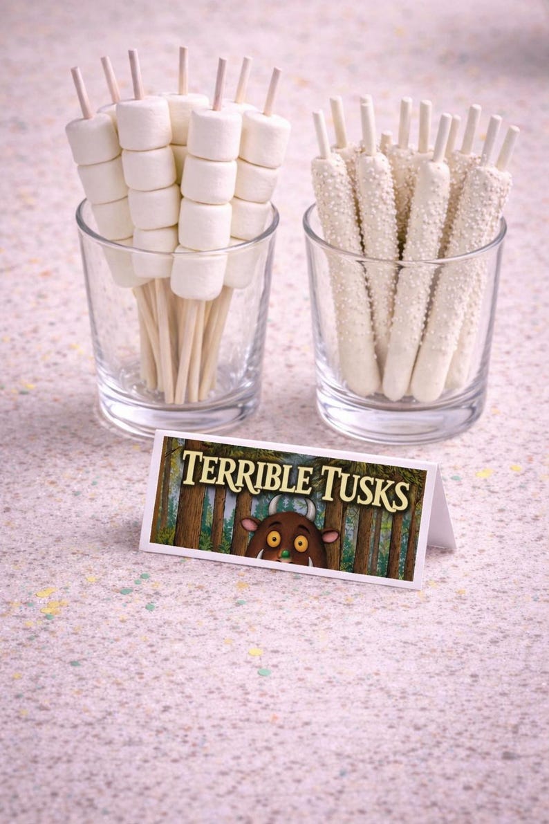 May include: Two clear glasses with treats. One glass holds marshmallow skewers, the other holds white chocolate-covered pretzel sticks. A small sign reads "TERRIBLE TUSKS" with a cartoon illustration.