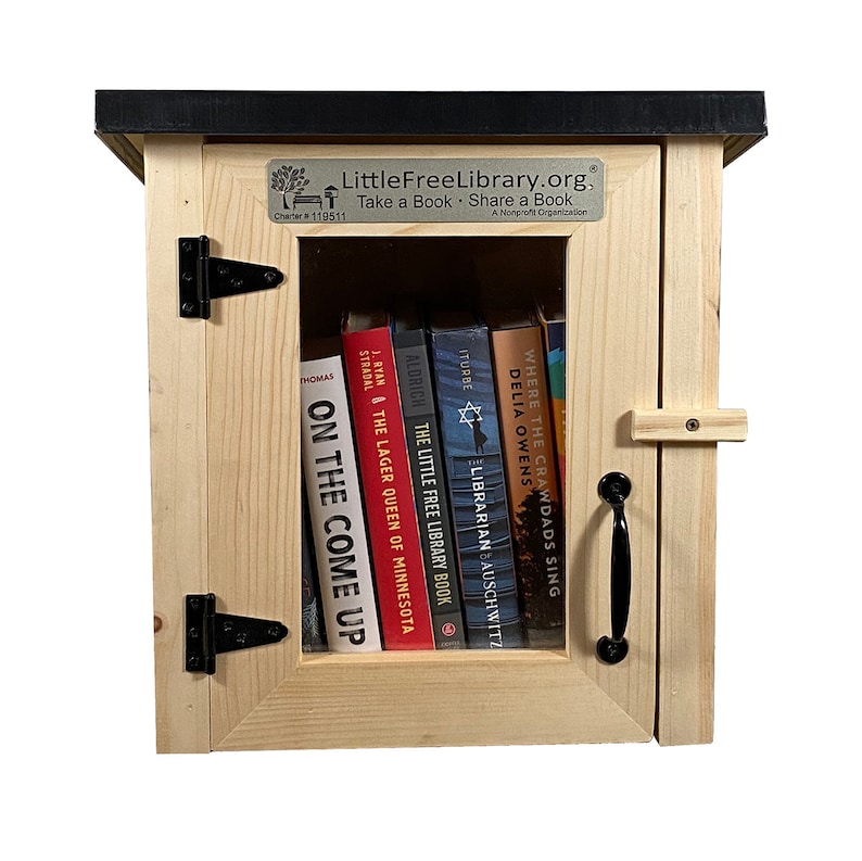 May include: A wooden Little Free Library with a black roof and a glass door. The door is open and there are several books on the shelves inside. The sign on the front of the library says "LittleFreeLibrary.org, Take a Book Share a Book, A Nonprofit Organization, Charter #119511."