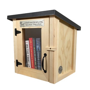 May include: A wooden Little Free Library book exchange box with a black roof. The box has a glass door and a shelf inside with several books. The sign on the front reads "LittleFreeLibrary.org. Take a Book Share a Book. A Nonprofit Organization."