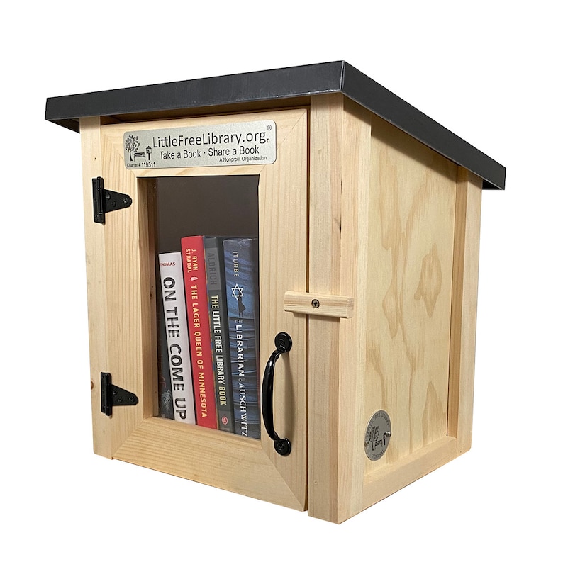 May include: A wooden Little Free Library book exchange box with a black roof. The box has a glass door and a shelf inside with several books. The sign on the front reads "LittleFreeLibrary.org. Take a Book Share a Book. A Nonprofit Organization."