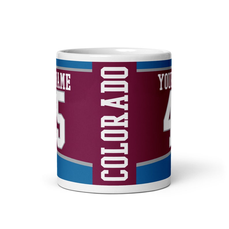 May include: White ceramic coffee mug with a burgundy, blue, and gray design. The mug features the word "COLORADO" in white lettering and a number "4" in gray lettering.