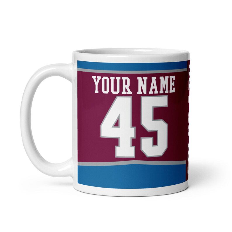 May include: White ceramic coffee mug with a burgundy, gray, and blue design. The mug has the text "YOUR NAME" and the number "45" printed on it.