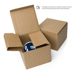 K&ouml;nnte beinhalten: Eine wei&szlig;e Keramiktasse mit einem blau-wei&szlig;en Design ist in einem braunen Karton verpackt. Der Karton ist ge&ouml;ffnet und die Tasse ist im Inneren sichtbar. Der Text auf der Tasse lautet "YOUR NAME".
