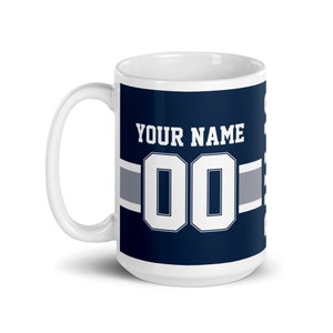 K&ouml;nnte beinhalten: Wei&szlig;e Keramiktasse mit blau-wei&szlig;em Design. Die Tasse zeigt ein Fu&szlig;balltrikot mit dem Text "YOUR NAME" und der Nummer "00".