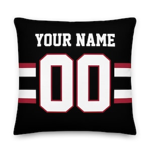 May include: Black and white pillow with a red and white stripe design. The pillow features a white number "00" and the text "YOUR NAME" in white.