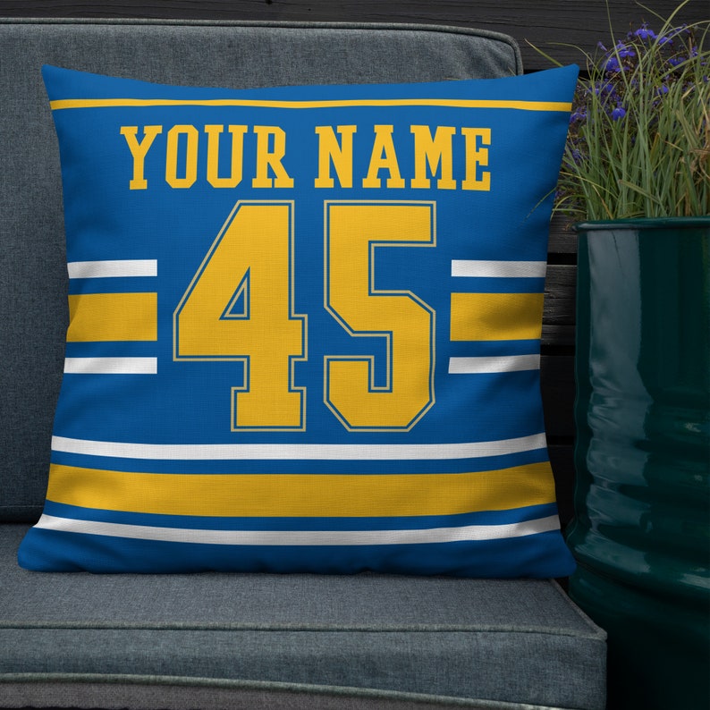 May include: Blue and yellow throw pillow with the text "YOUR NAME" and the number "45" in a jersey style font.