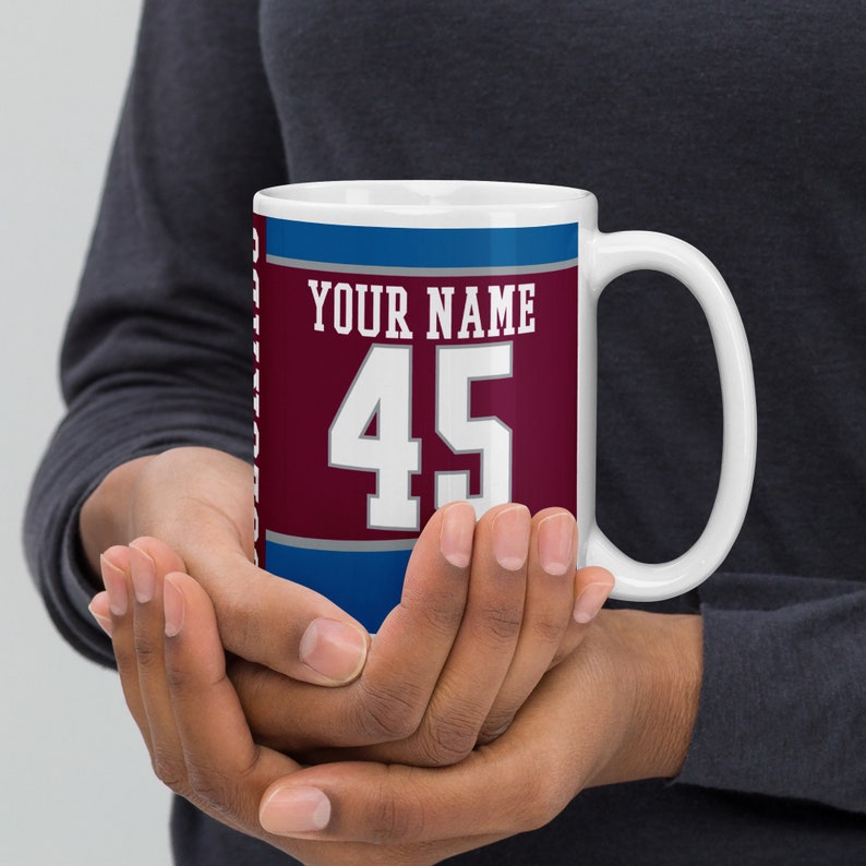 May include: White ceramic mug with a burgundy, blue, and white design. The mug has the text "YOUR NAME" and the number "45" printed on it.