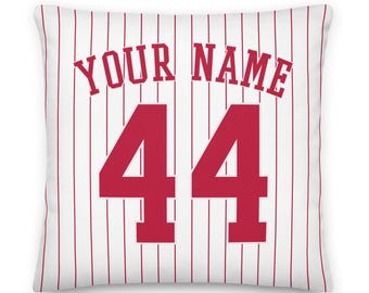 May include: A square throw pillow featuring a white background with vertical red pinstripes. The text YOUR NAME is printed in a red athletic font above the large red number 44, which is centered on the front of the pillow cover.