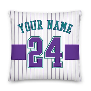 Könnte beinhalten: Weißes Kissen mit einem Baseballtrikot-Design. Das Trikot hat violette und türkisfarbene Streifen, eine violette Nummer 24 und den Text "YOUR NAME".