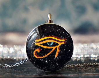 May include: A silver chain necklace with a round pendant featuring a black background with gold glitter and a colorful depiction of the Eye of Horus.