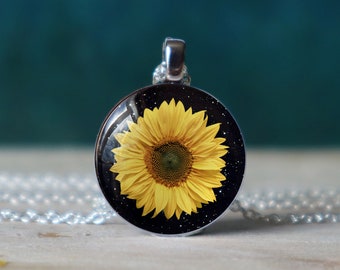 May include: A silver necklace with a round pendant featuring a yellow sunflower on a black background with white speckles.