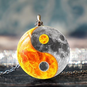 May include: A silver chain necklace with a round pendant featuring a yin yang symbol. The yin side is depicted as a black and white moon, while the yang side is a fiery orange sun.