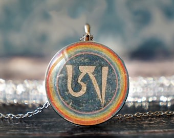 May include: A silver chain necklace with a round pendant featuring a rainbow border and a blue background with a white symbol in the center. The symbol is a stylized "Om" in Sanskrit.