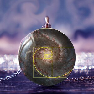 Peut inclure: Un collier en argent avec un pendentif rond représentant une image de galaxie avec une spirale de Fibonacci jaune superposée.