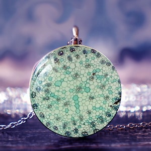 May include: A silver chain necklace with a round pendant featuring a green and white abstract pattern. The pendant is made of resin and has a glossy finish.