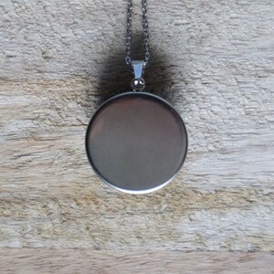 Puede incluir: Un collar de plata con un colgante redondo liso de plata. El colgante est&aacute; en blanco y tiene un acabado brillante.