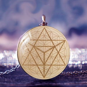 May include: A silver chain necklace with a round pendant featuring a gold geometric design, known as the Flower of Life, on a white background.
