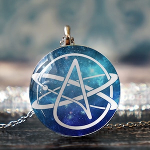 May include: A silver chain necklace with a round pendant featuring a white stylized 'A' inside a circle with a galaxy background.