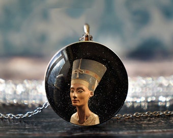 May include: A silver chain necklace with a round pendant featuring a black and white image of an Egyptian queen wearing a tall headdress.