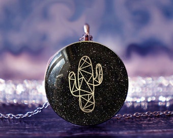 May include: A silver chain necklace with a round black pendant featuring a gold geometric cactus design on a glittery background.