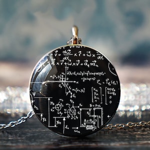 Puede incluir: Un collar de cadena de plata con un colgante redondo negro con ecuaciones y diagramas matemáticos blancos. El colgante es una cúpula de vidrio con fondo negro.