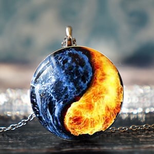 May include: A silver chain necklace with a round pendant featuring a yin yang design. The pendant has a blue and white swirl on one side and a yellow and orange swirl on the other side.