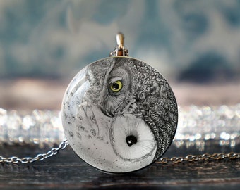 May include: A silver chain necklace with a round pendant featuring a black and white drawing of an owl with a yellow eye. The owl is depicted in a yin yang design.