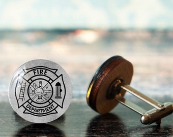 May include: Silver cufflinks with a black and white fire department logo. The logo features a fire hydrant, an axe, a helmet, and a ladder. The cufflinks have a wooden backing.