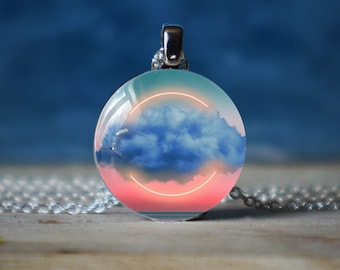 May include: A silver chain necklace with a round pendant featuring a blue cloud against a pink and blue sunset with a neon pink circle.
