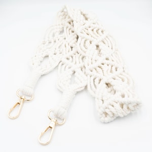 Può includere: Tracolla per borsa in crochet bianco con fibbie in metallo dorato. La tracolla è realizzata con un cordoncino spesso e testurizzato e presenta un design delicato e intricato.