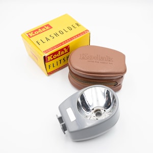 May include: A vintage Kodak Flasholder with a brown leather case and a gray flash unit. The box is yellow with black text that reads "Kodak Flasholder Specially Made for Kodak"